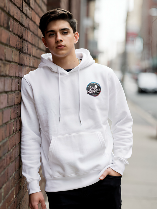 Person wearing a white hoodie with a logo, leaning against a brick wall on a street.