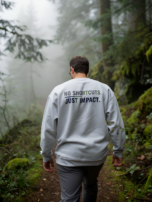 Person wearing a sweatshirt with 'No Shortcuts. Just Impact.' in a forest